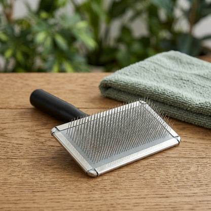 Brosse carde pour chien à picots fins en acier inoxydable et manche noir, posée près d'une serviette