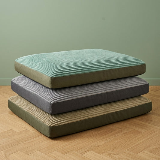 Coussin pour chien en velours côtelé, coloris vert, gris et kaki, empilés sur un parquet