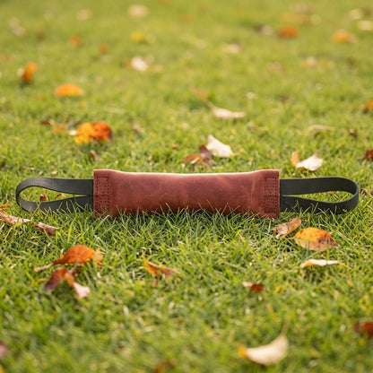 Jouet indestructible pour chien : boudin de traction en cuir rouge brique à deux poignées, posé dans l'herbe
