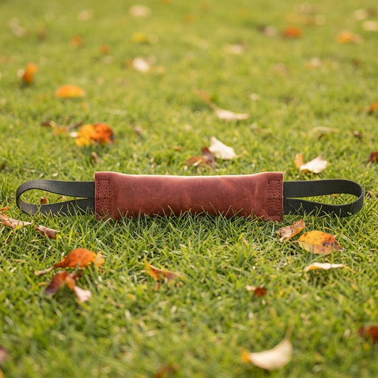 Jouet indestructible pour chien : boudin de traction en cuir rouge brique à deux poignées, posé dans l'herbe