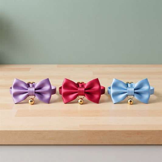 Nœud papillon pour chien à clochette en violet, rouge et bleu ciel, posés sur un plan de travail