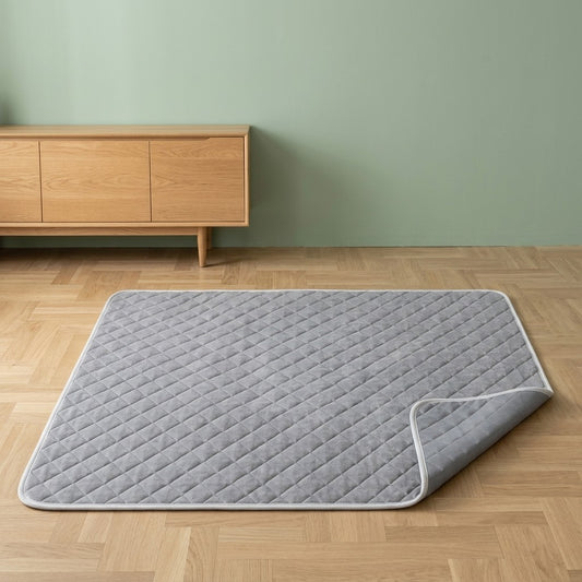 Tapis rafraîchissant pour chien gris matelassé à liseré blanc, un coin replié, sur un parquet